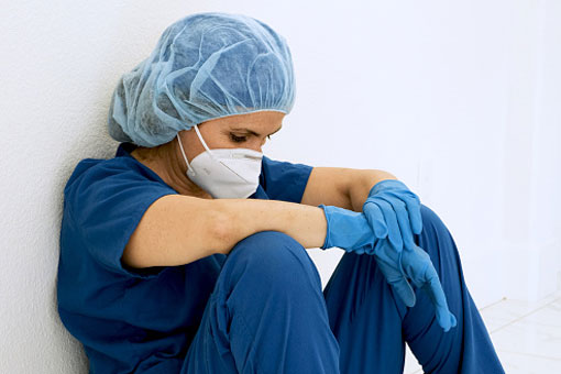 Nurse exhausted and in scrubs with gloves and mask on